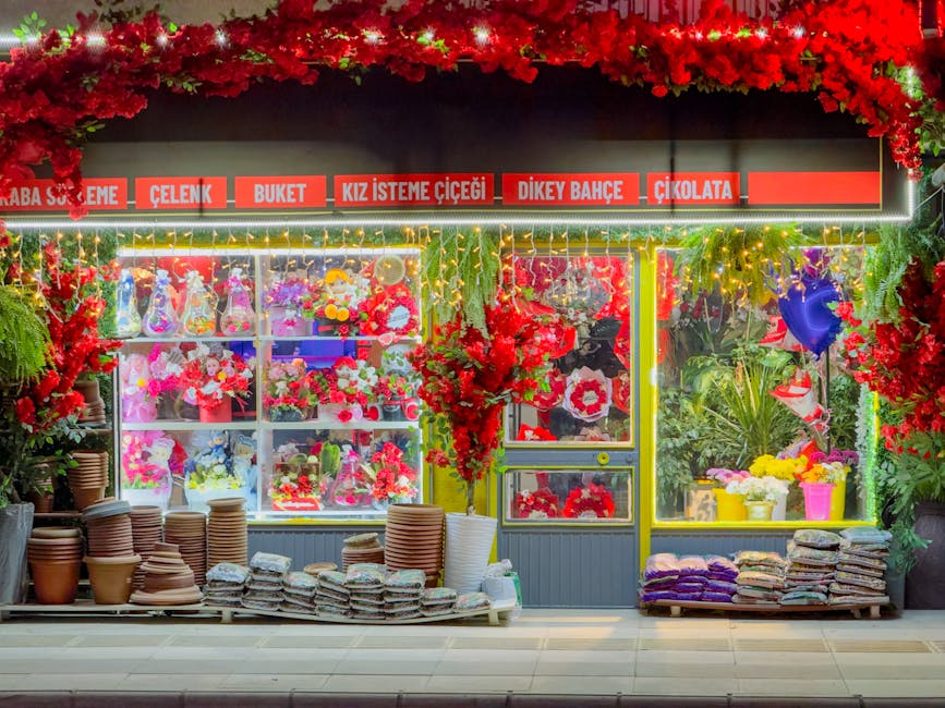 A vibrant floral shop showcasing a variety of fresh flowers and floral arrangements inside and outside a storefront. The display case is filled with colorful bouquets of pink, red, purple, and white f
